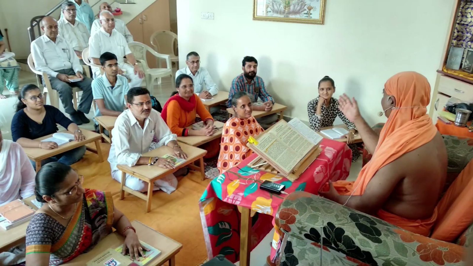 Swami ji mid-discourse, teaching a group of students from an open text